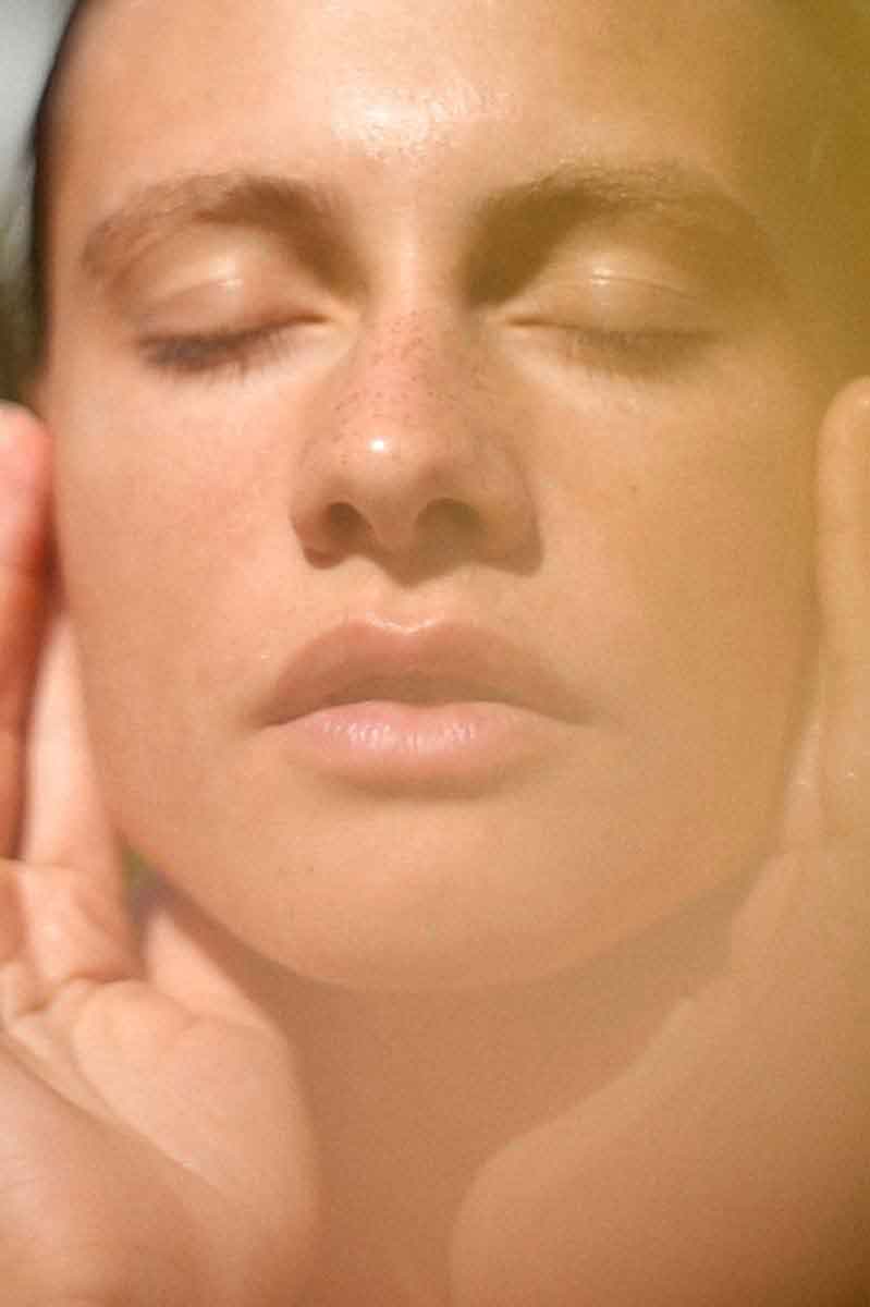 image of a woman in the nature applying her skincare routine with fields of yarrow products