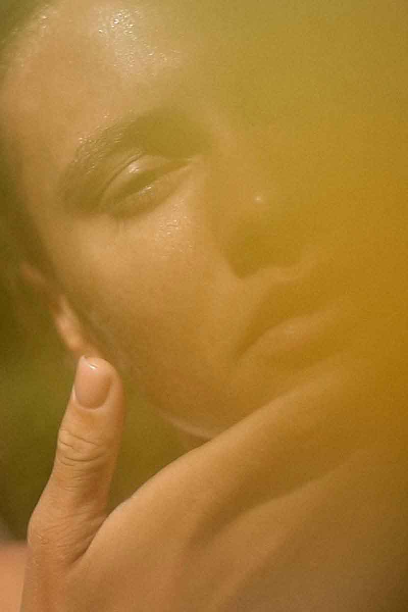 decorative image of a woman in the nature applying her skincare routine with fields of yarrow products