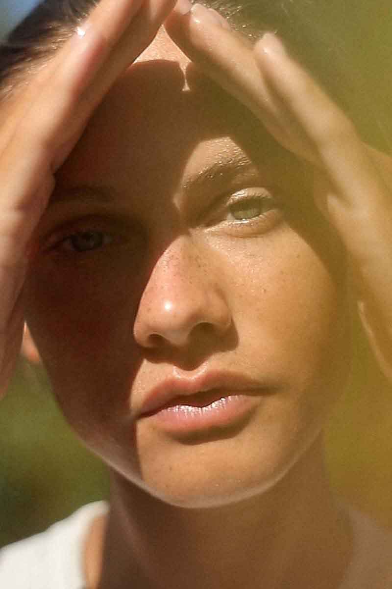 image of a woman in the nature applying her skincare routine with fields of yarrow products with her hands on her face