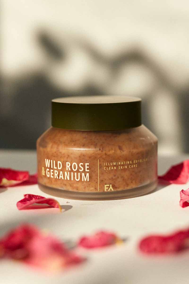 wild rose and geranium illuminating exfoliant jar on a tabletop with rose petals