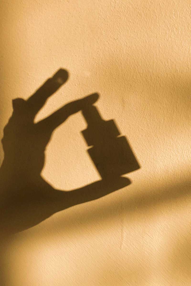 Shadow of a woman's hand holding a fields of yarrow skincare product